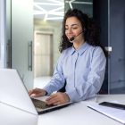 Successful hispanic woman with headset phone for video call working with laptop while sitting at